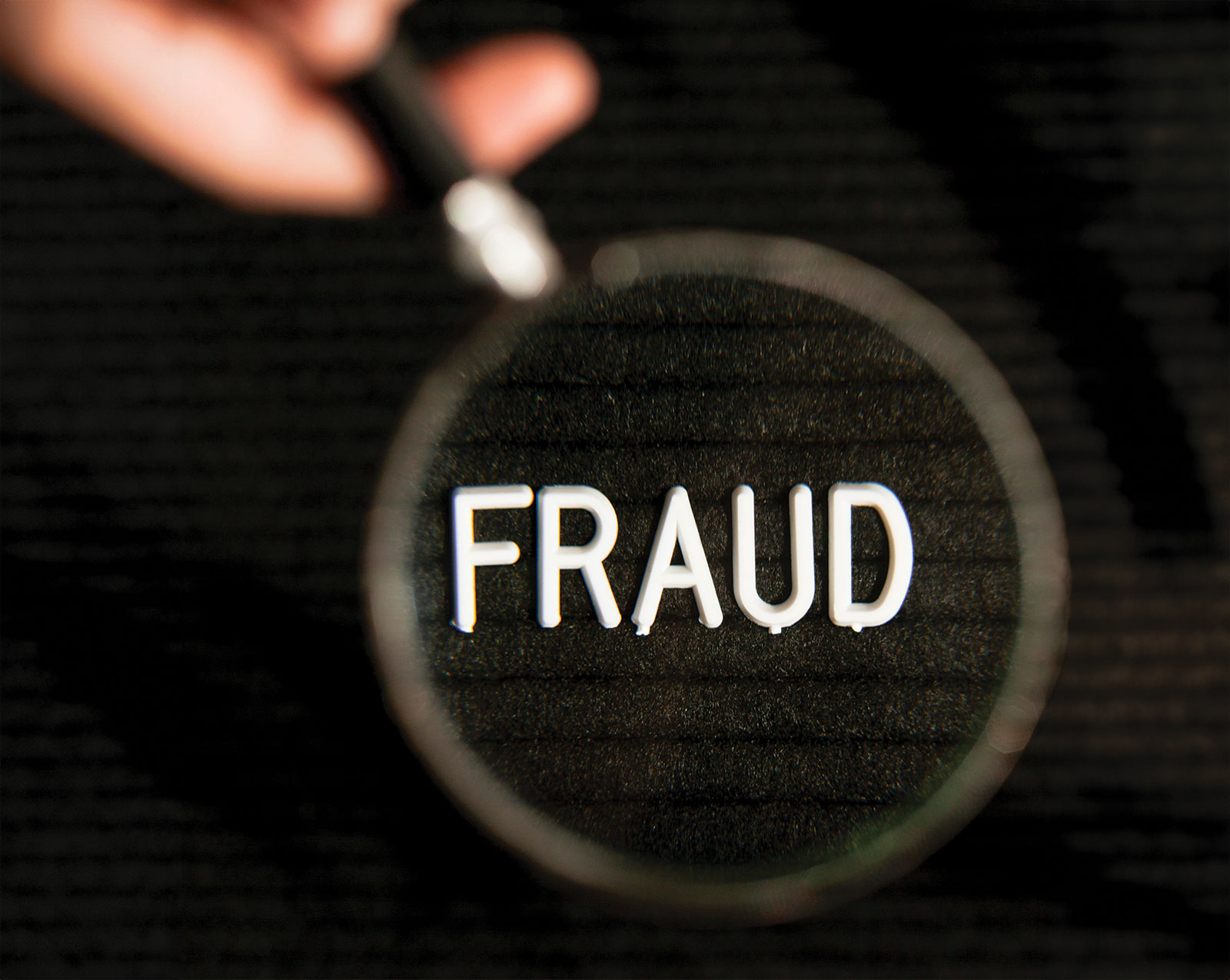 Magnifying glass held over the word "FRAUD"