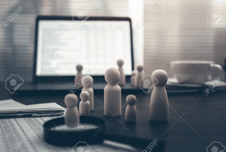 Wooden figures representing a team beside a laptop on a desk